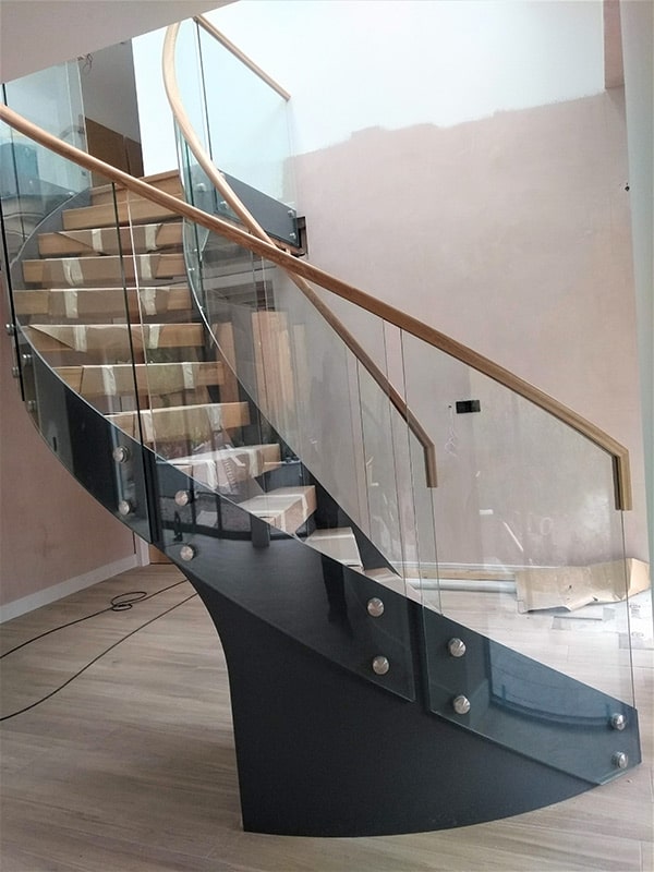 Curved glass balustrade with wooden banister around spiral staircase