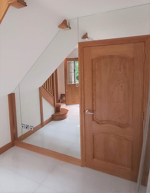 Wooden door surrounded by a custom cut mirror that is cut around the room's angles
