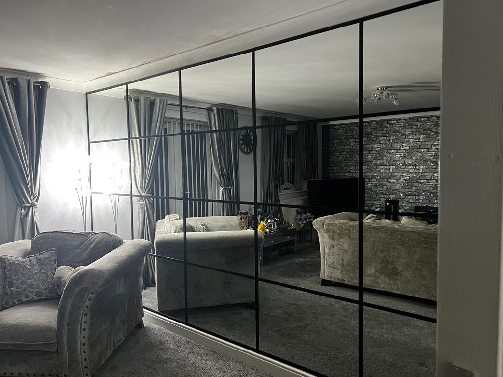 Wall length custom cut mirror with black square lines reflecting living room sofas and wall